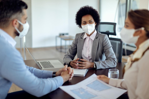 Zwarte makelaar die een gezichtsmasker draagt tijdens een ontmoeting met haar klanten op kantoor