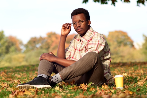 Zwarte man, afro-amerikaanse man die in het gouden herfstpark loopt in de herfst met een koffiekopje