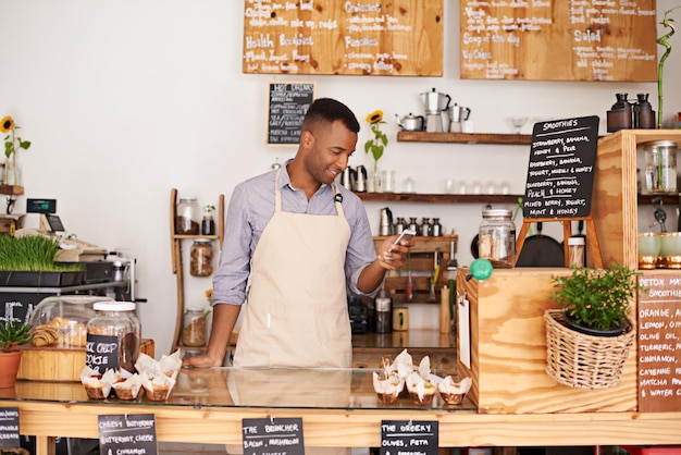 Zwarte man coffeeshop en winkeltelefoon van een ondernemer met geluk van kleine bedrijven Cafe mobiel en barista kijken naar online app met een glimlach bij bakkerij en restaurant voelen zich gelukkig