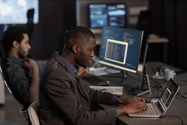 Zwarte man die code schrijft en typt op het toetsenbord van de laptop