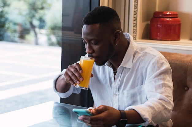 Zwarte man die op de telefoon surft in een café terwijl hij sinaasappelsap drinkt