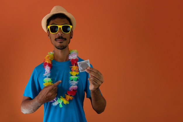 Zwarte man in kostuum voor brazilië carnaval met een condoom geïsoleerd op een oranje achtergrond. afrikaanse man in verschillende poses en uitdrukkingen.