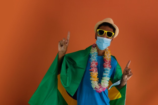 Zwarte man in kostuum voor carnaval met braziliaanse vlag en pandemisch masker geïsoleerd op een oranje achtergrond. afrikaanse man in verschillende poses en uitdrukkingen.