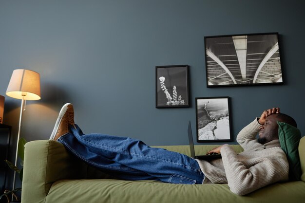 Foto zwarte man ligt op de bank met een laptop.