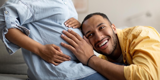 Zwarte man luistert naar zwangere vrouw's buik binnen Panorama bijgesneden