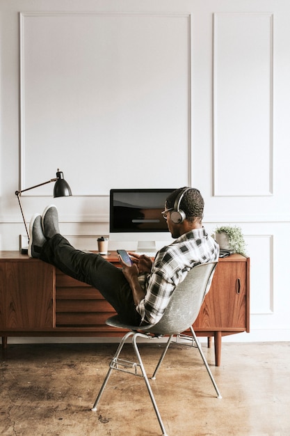 Zwarte man met koptelefoon die op zijn telefoon aan zijn bureau zit