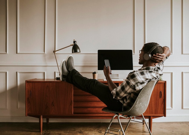 Zwarte man met koptelefoon die op zijn telefoon aan zijn bureau zit