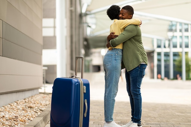 Zwarte man ontmoet vrouw in luchthaven knuffelen staande binnen
