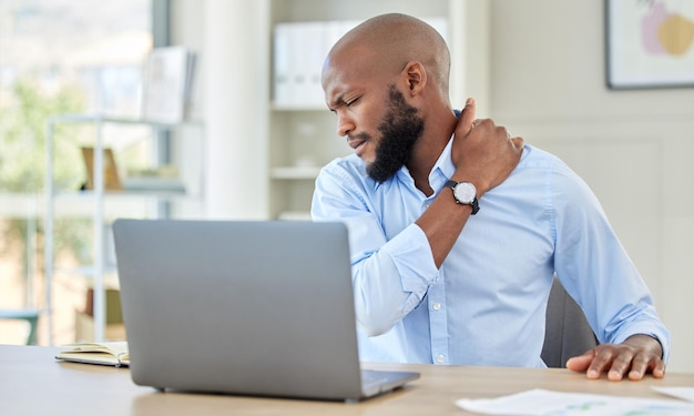 Zwarte man schouderpijn op laptop bij stress en letsel die lijden aan overbelasting thuis Gestresste Afrikaanse man met pijnlijke spierspanning of gewrichtsontsteking zittend met computer en werk