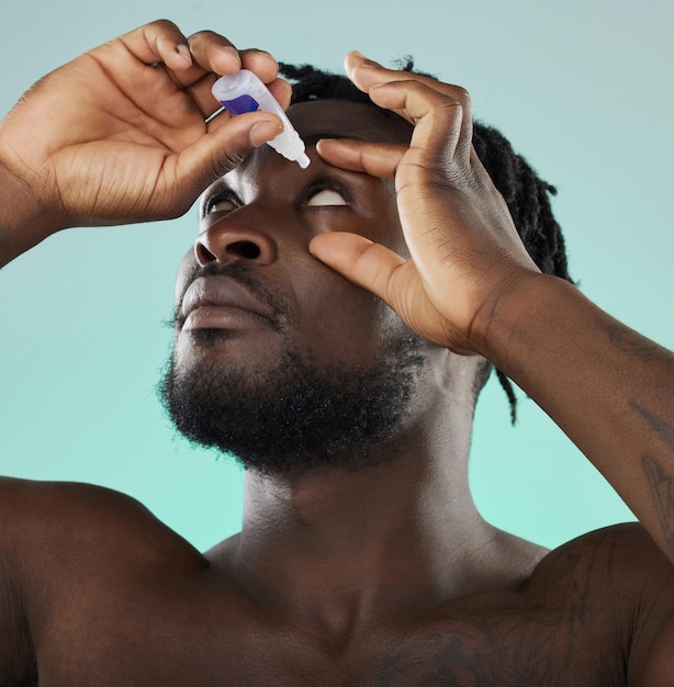 Zwarte man studio en oogdruppel voor gezondheidsvisie wellness en zelfzorg door blauwe achtergrond voor ochtendroutine Afrikaanse gen z model ogen en product voor gezondheidszorggeneeskunde en medische serumfles
