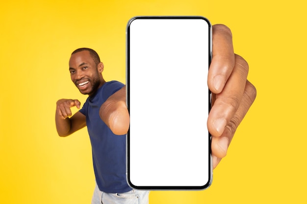 Zwarte man toont mobiele telefoon met een enorm leeg scherm gele achtergrond