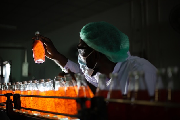 Foto zwarte mannelijke arbeider die sapfles op bottellijn inspecteert bij een drankfactor