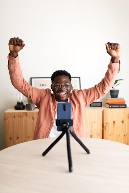 Foto zwarte mannelijke influencer live streaming met mobiele telefoon vieren succes met zijn volgelingen vertical