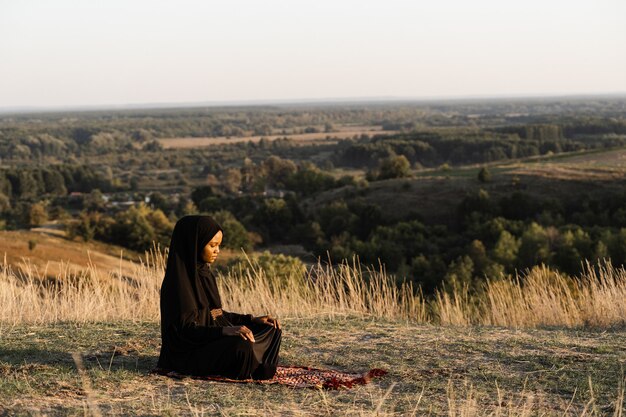 Zwarte moslimvrouw die op het tapijt bidt. Solat bidden op de prachtige heuvel. Salah traditioneel bidden.