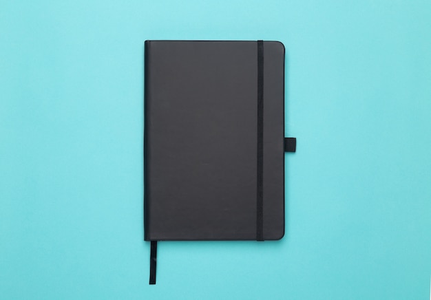 Zwarte notebook geïsoleerd op blauwe plat lag of bovenaanzicht hoek.