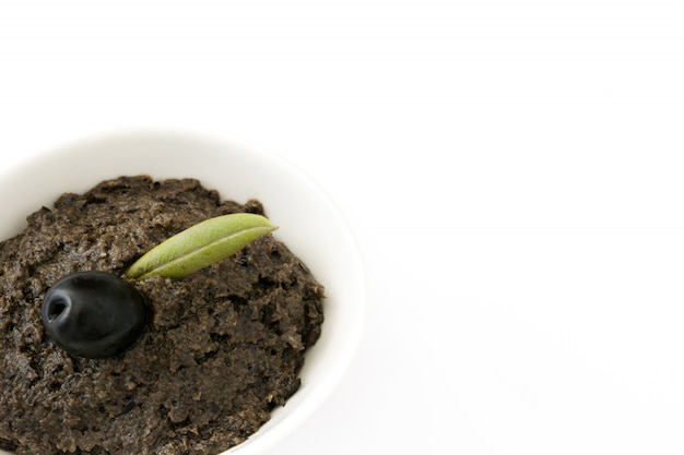 Zwarte olijventapenade met ansjovis, knoflook en olijfolie die op wit wordt geïsoleerd