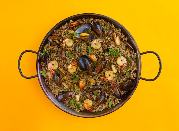 Zwarte paella met rijstgarnalen, mosselen en inktvisinkt op gele achtergrond