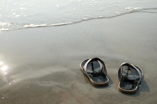 Zwarte pantoffels die op het natte zand bij het water staan