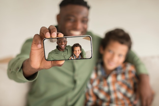 Zwarte papa en zoontje met smartphone die selfies binnen maken