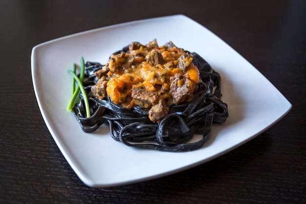 Zwarte pasta met inktvisinkt pasta van durumtarwegriesmeel met inktvisinkt met rundvlees en paprikasaus op een vierkant bord versierd met groene uien