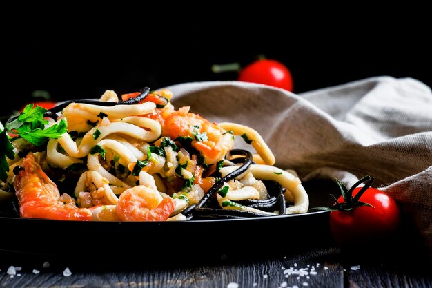 Zwarte pasta met zeevruchten en tomatensaus op een plaat zwarte achtergrond selectieve focus