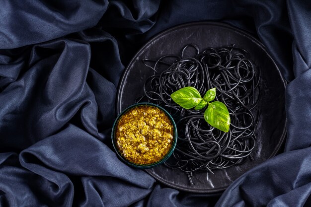 Zwarte pasta, pestosaus en basilicum op een donkere ondergrond