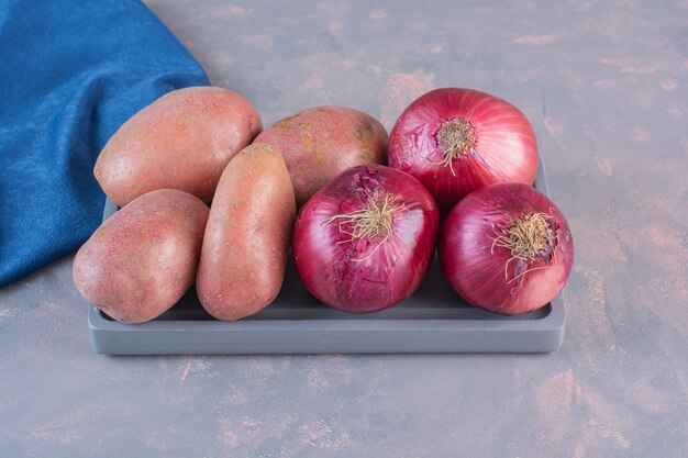 Zwarte plaat van zoete aardappelen en rode uien op stenen achtergrond.