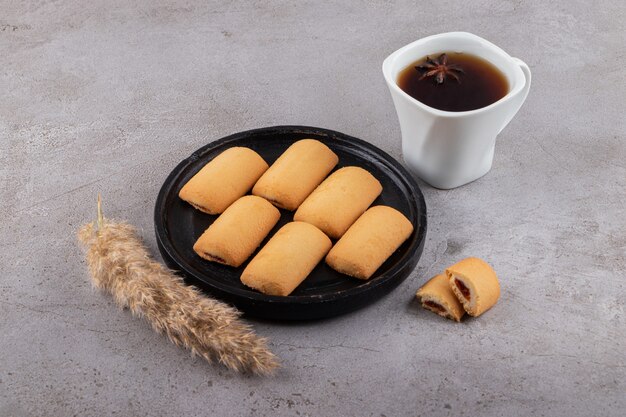 Zwarte plaat van zoete koekjes en kopje thee op stenen tafel.