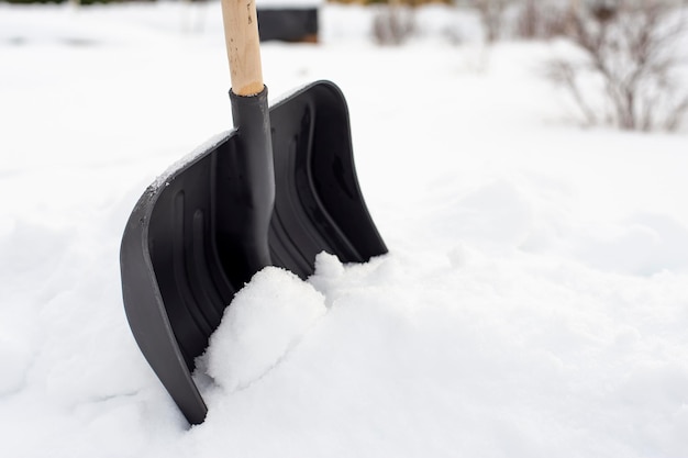 Zwarte plastic schop met een houten handvat die in een sneeuwbank staat