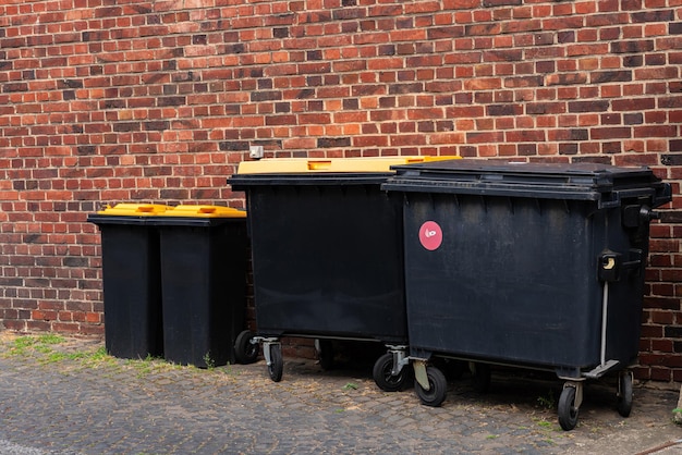 Zwarte plastic vuilnisbakken met gele deksels naast de muur van een bakstenen gebouw