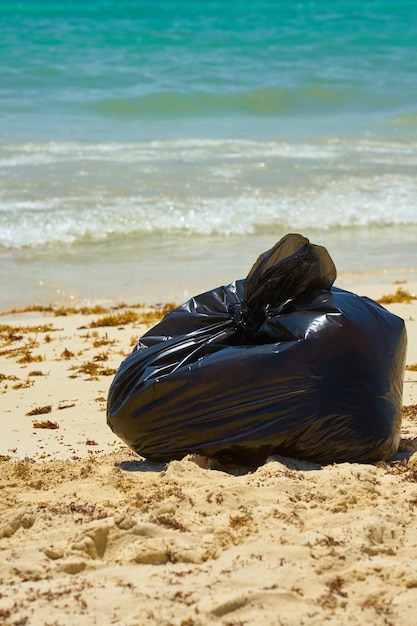 Zwarte plastic vuilniszak op een zandstrand met een tropische zee op de achtergrond