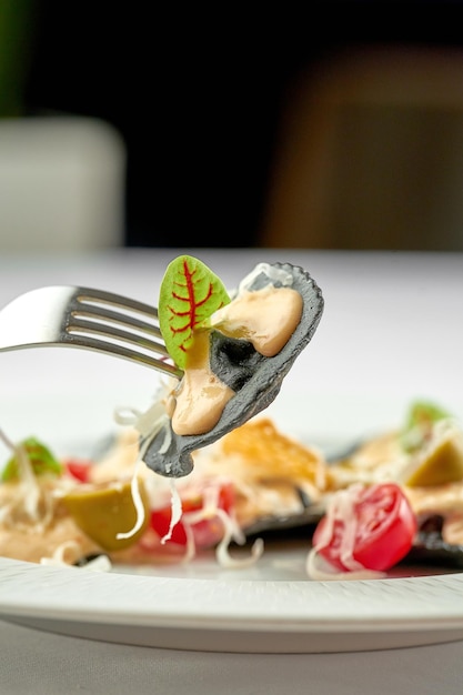 Zwarte ravioli met vlees gestoken op een vorksaus en tomaten in een bord