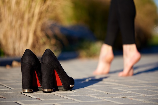 Zwarte schoenen op de weg op vrouwelijke benen blootvoets als achtergrond.