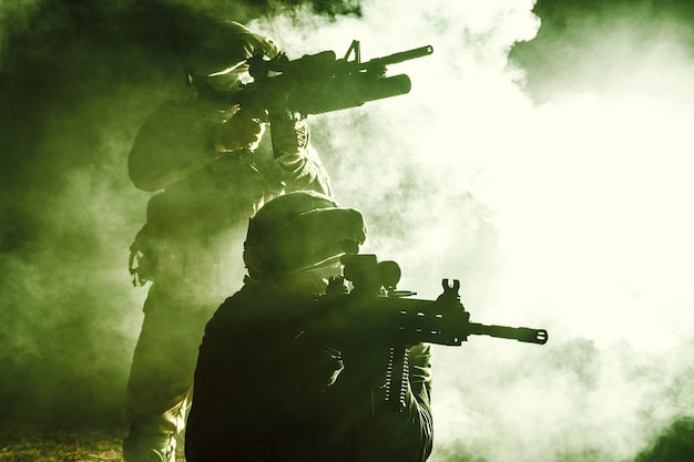 Zwarte silhouetten van een paar soldaten in de rook die zich verplaatsen in de strijd. Tegenlicht, bijgesneden, afgezwakt en ingekleurd