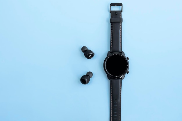Foto zwarte smartwatch en draadloze koptelefoon op een blauwe achtergrond blanco scherm kopie ruimte