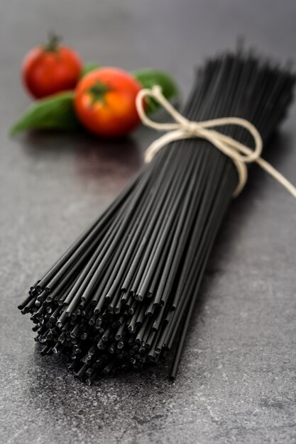 Foto zwarte spaghetti, basilicum en tomaten op zwarte leiachtergrond