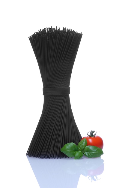 Zwarte spaghetti met baselblaadjes en rode tomaat op witte muur.