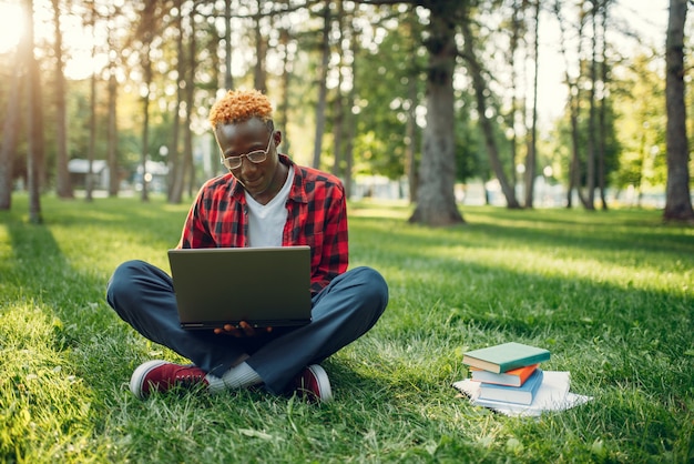 Zwarte student met laptop zittend op het gras in zomerpark. Een tiener die studeert en zich buiten ontspant