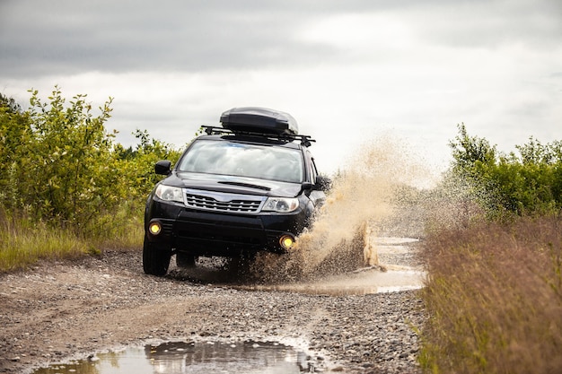 Zwarte Subaru Forester rijden op een onverharde weg met plassen. Water spat onder de wielen vandaan