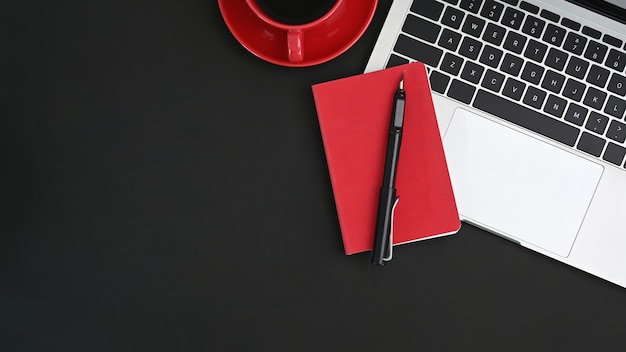 Zwarte tafel met laptop, pen, koffie en notitieboekje. Bureauconcept.
