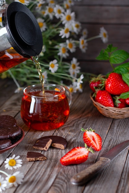 Zwarte thee in een glazen beker op een houten tafel met chocoladeschilferkoekjes en aardbeien. verticaal