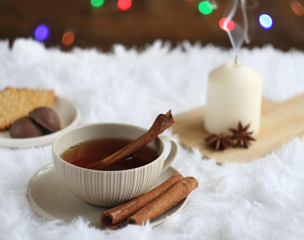 Foto zwarte thee in een mok staat op een pluizige plaid achter het bord met een nieuwjaarsslinger er is een kaars in de buurt, snoep, kaneelstokjes en anijsleugen