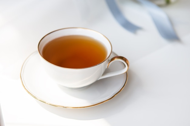 Zwarte thee in een porseleinen mooie witte kop met een gouden snede. Mooie zonneschijn. Thee ceremonie.