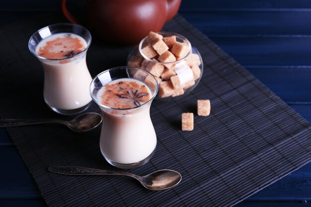 Zwarte thee met melk in glazen en theepot met forfaitaire suiker op bamboe mat en houten planken achtergrond kleur