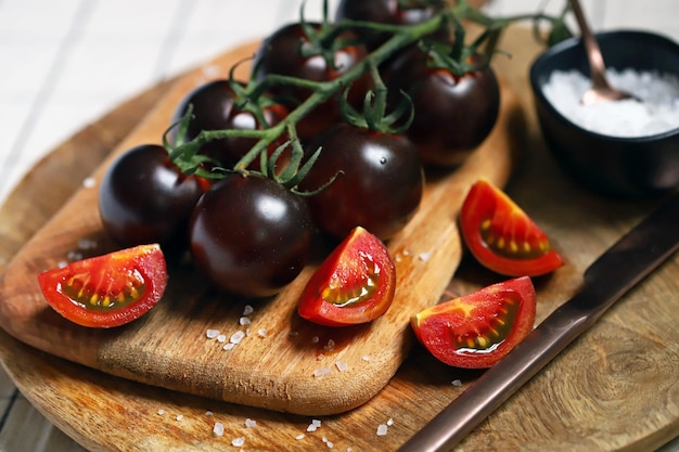 Zwarte tomaten op een tak op een houten bord met zeezout