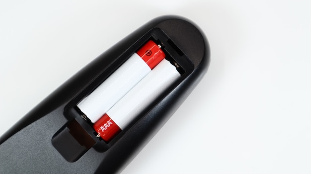 Zwarte tv-afstandsbediening met AAA-alkalinebatterijen in rood en wit op een witte achtergrond. Vervanging van de batterij, reserveonderdelen. Afstandsbediening batterijcompartiment close-up. Ruimte kopiëren.
