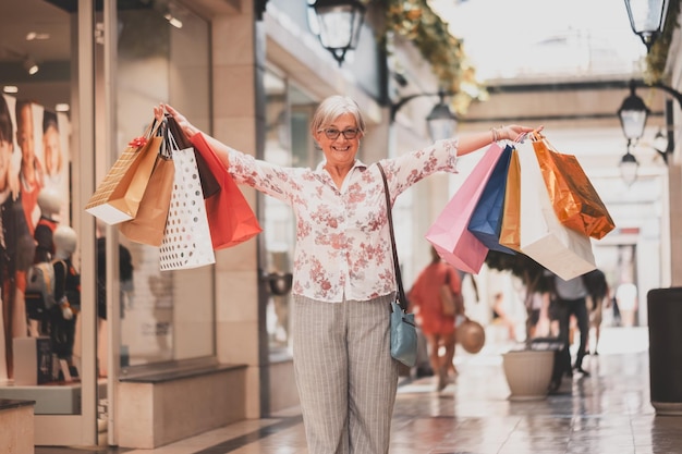 Zwarte vrijdag winkelen voor aantrekkelijke lachende oudere vrouw met boodschappentassen die gelukkig kijken naar het concept van cameraconsumentisme