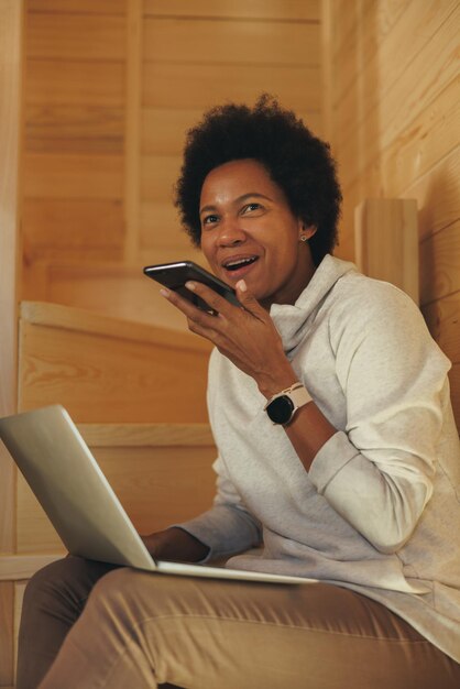 Zwarte vrouw die een audiobericht verzendt op een smartphone tijdens het gebruik van een laptop tijdens de vakantie.