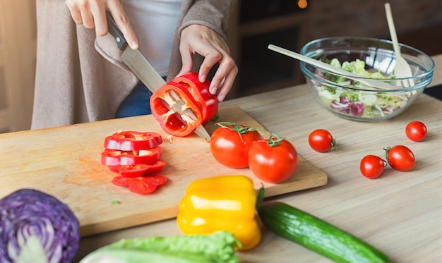 Zwarte vrouw die groenten snijdt voor gezonde vegetarische salade in keuken, close-up, crop