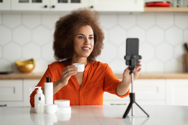 Zwarte vrouw die huidverzorgingsproduct naar de camera laat zien terwijl ze thuis video opneemt